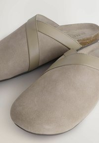 Bēša zamšādas slip-on apavi ar gludu ādas akcenta siksnu. Apaļa purngala un zema profila dizains, ar korķa tipa zolīti.