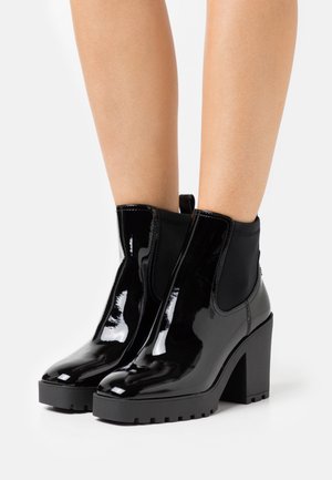 Black patent leather ankle boots with a chunky black heel, elastic side panels, and a smooth, shiny finish. A tab pull at the back.