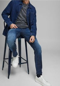 Mörkblå jeansjacka över en grå t-shirt, kombinerad med blå jeans och vita sneakers. Bekväm passform med klassiska designelement.