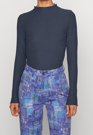 Haut côtelé bleu foncé à manches longues associé à un pantalon taille haute bleu et violet avec un motif œil numérique.