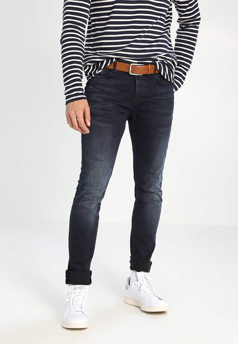 Jeans blu scuro con vestibilità slim, dettagli sbiaditi e orli arrotolati. Abbinati a una camicia a righe a maniche lunghe e sneakers bianche. Cintura marrone.