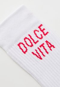 Biela bavlnená ponožka s červeným vyšívaným nápisom "DOLCE VITA". Dizajn obsahuje rebrovanú textúru a lem na vrchu.