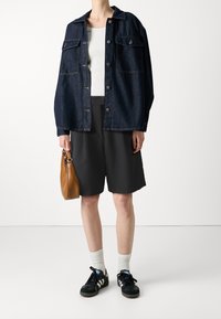 Dżinsowa kurtka, ciemnoniebieska, z kieszeniami na piersi i metalowymi guzikami. Biała koszula, czarne szorty, czarne trampki z białymi paskami, brązowa torebka.