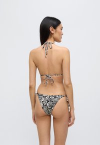 Μπικίνι σε ασπρόμαυρο με ανθικό γραφικό σχέδιο· λαιμόκοψη halter και ρυθμιζόμενες κορδόνες. Το υλικό φαίνεται υφασμάτινο, με χαμηλή γραμμή στα κάτω μέρη.