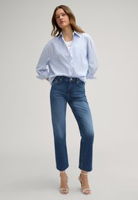 Hellblaues Hemd, lässige Passform; dunkelblaue cropped Jeans mit fransigem Saum; klare Riemchen-High-Heels.