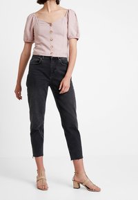 Blusa rosa con maniche a palloncino e chiusura a bottoni, abbinata a jeans neri a sigaretta e sandali beige con tacco a blocco. Tessuto liscio, silhouette aderente.