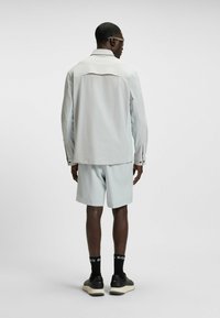 Light grey jacket with long sleeves and collar, paired with matching shorts. Material appears smooth, with subtle texture and fitted design.