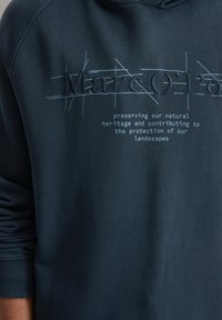 Sweat-shirt bleu foncé avec broderie à l'avant, arborant "Marc O'Polo" et un texte sur le patrimoine naturel en bleu clair contrastant.