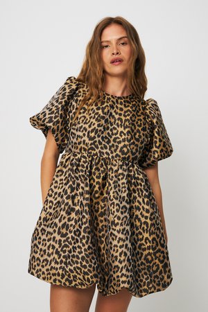 Γυναίκα που φοράει ένα κοντό φόρεμα με φουσκωτά μανίκια και καφέ-μαύρο μοτίβο λεοπάρ, μπροστά σε απλό φωτεινό φόντο.