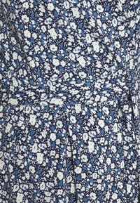 Tissu à motif floral bleu et blanc avec de petites fleurs et une ceinture en tissu assortie nouée à la taille.