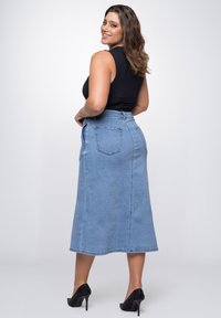 Lichtblauwe denimrok met een rechte midi-snede, voorzien van twee achterzakken en een subtiele vervaagde textuur. G combinéerd met zwarte hoge hakken.