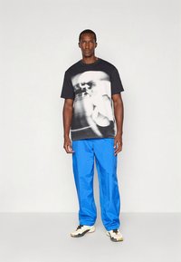 Czarno-biała koszulka z grafiką z rozmytym wzorem, zestawiona z niebieskimi, luźnymi spodniami i neutralnymi tenisówkami.