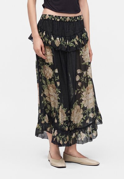 Μαύρη διαφανής midi φούστα με floral μοτίβο και βολάν, φορεμένη με μπεζ επίπεδα παπούτσια, εμφανίζεται σε μοντέλο από τον κορμό έως τα πόδια.