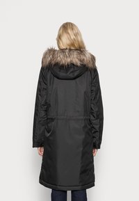 Zwarte parka met een bontgevoerde capuchon, lange mouwen en een aangesloten taille. Heeft een gladde textuur en drukknoopdetails aan de zoom.