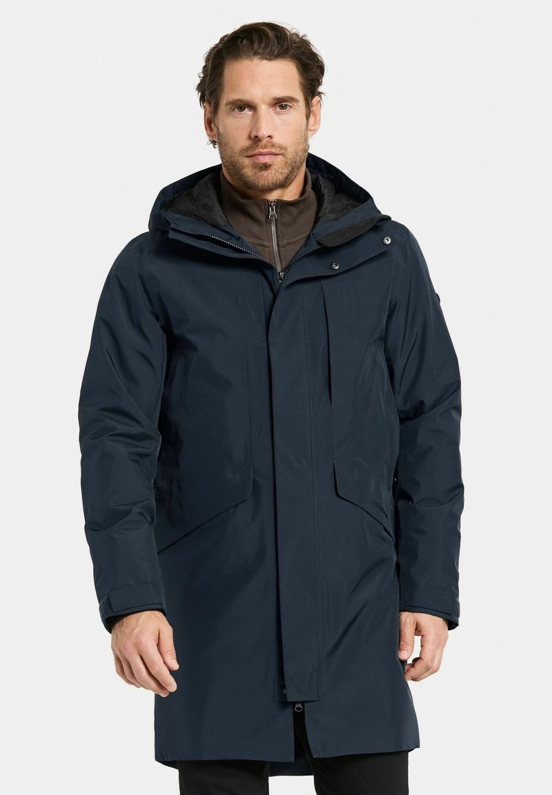 Mörk marinblå vattentät parka med huva, framzippering och två stora sidofickor. Har en mjuk innerfoder och justerbara ärmslut.