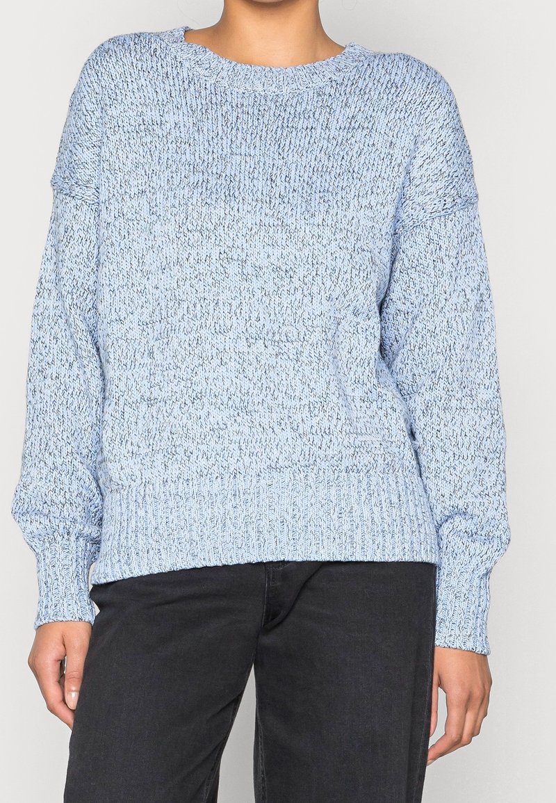 Light blue knitted sweater with a textured design, ribbed hem, and wide sleeves. Material appears soft and slightly loose-fitting.