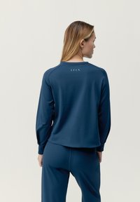 Marinblå långärmad topp i ett mjukt tyg, med rund halsringning och detalj på baksidan med små utskärningar. Matchas med byxor i samma färg.