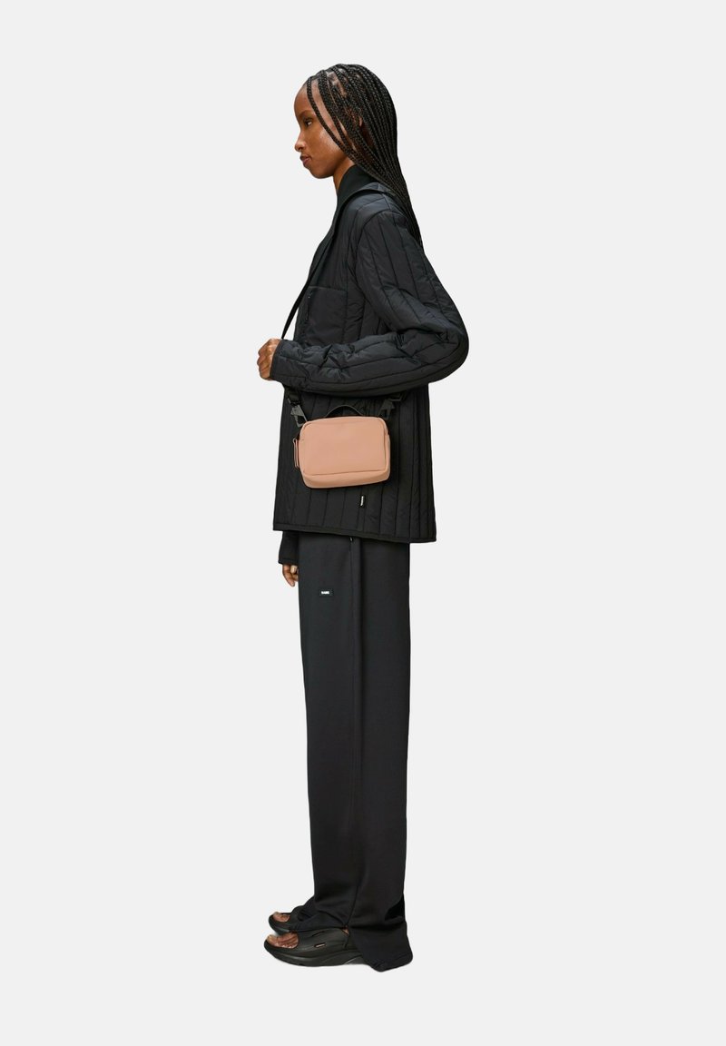 Giacca nera trapuntata, pantaloni neri larghi e borsa a tracolla marrone. Il modello indossa sandali neri. Design minimalista, look monocromatico.