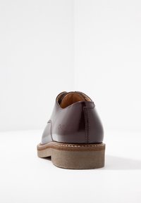Dunkelburgunderfarbene Lederschuhe mit glatter Oberfläche, runder Zehenpartie und beige strukturiertem Sohlenmaterial. Mit eingeprägtem Logo auf der Ferse.