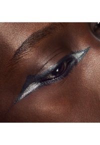 Gros plan sur un œil à la peau foncée avec un eye-liner angulaire argenté et noir audacieux s'étendant du coin interne au coin externe.