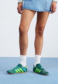 Grønne atletiske sko med gule striber, tekstureret syntetisk materiale, rund tå, gummisål, stylet med hvide sokker og en denimnederdel.