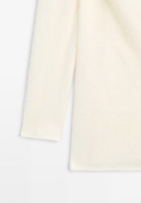 Pull crème fabriqué en tissu doux, avec des manches longues et une coupe décontractée, doté d'une texture lisse et sans motifs ni accents visibles.
