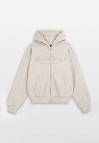 Beżowa bluza z kapturem na zamek, z przednią kieszenią typu kangur, kapturem ze sznurkiem i napisem "INFLAMMABLE" w kontrastowym kolorze na piersi.