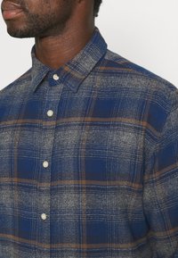 Blå och grå rutig skjorta med knäppbar krage, med en mjuk textur och subtila bruna linjer, tillverkad av vävd tyg med knappar.