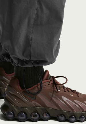 Gros plan sur le pied d'une personne portant des baskets Nike Air marron foncé avec des semelles à bulles d'air noires et un pantalon noir avec des poignets élastiques.