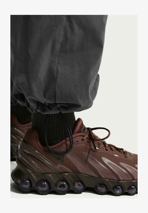 Primer plano del pie de una persona que lleva zapatillas Nike Air marrón oscuro con suelas negras de burbujas de aire y pantalones negros con puños elásticos.