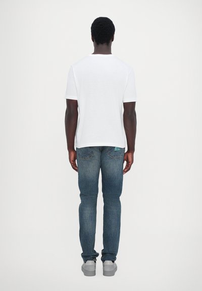 Tricou alb cu mânecă scurtă, blugi albaștri, adidași gri. Accent pe un design simplu, croială dreaptă și culoare solidă fără modele vizibile.