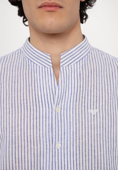 Modra in bela pajkasta srajca s stojčkom, gumbnim zapiranjem in vezenimi detajli, ki prikazujejo ozke vertikalne črte. Teksturirana tkanina.