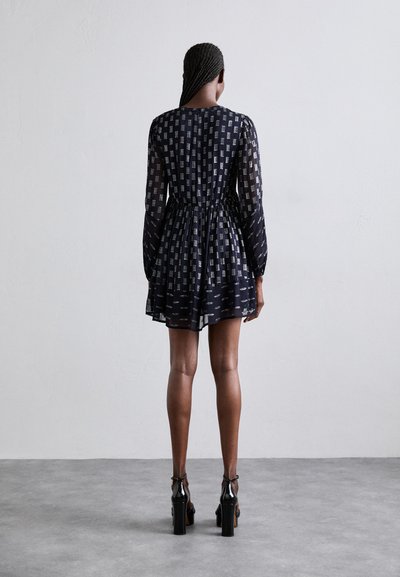Navyblaues Kleid mit langen, durchsichtigen Ärmeln und gerafftem Bund, das ein gemustertes Design aufweist. Kombiniert mit schwarzen High Heels.