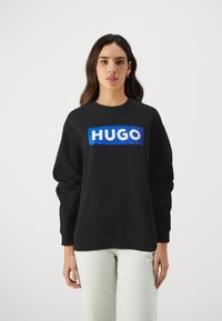 Čierny sveter s modro-bielym logom "HUGO" na prednej strane. Obsahuje okrúhly výstrih a dlhé rukávy. Mäkko, textúrované tkanivo.