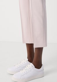 Witte veterschoenen van leer met een gladde afwerking, voorzien van gouden accenten, gecombineerd met lichtroze, op maat gemaakte capri-broeken.