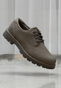 Brauner Leder-Schnürschuh für die Freizeit mit robustem Sohlenaufbau, Timberland-Logo auf der Ferse, fotografiert in der Luft vor einem hellen Hintergrund.
