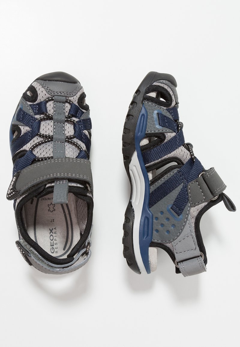 Sandalias Geox en gris y azul marino con materiales de textil y goma. Cuentan con correa ajustable, diseño de punta abierta y acentos de malla transpirable.