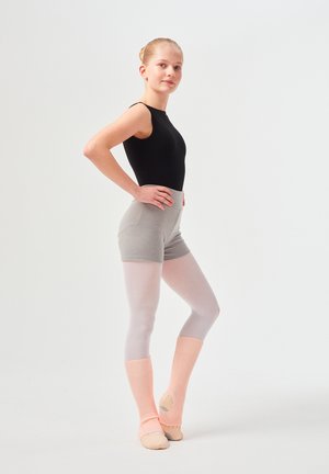 Schwarzer ärmelloser Body, graue gerippte Shorts, weiße Strumpfhosen und hellrosa Beinschoner mit offenem Fersendesign. Das Model posiert mit den Händen auf den Hüften.