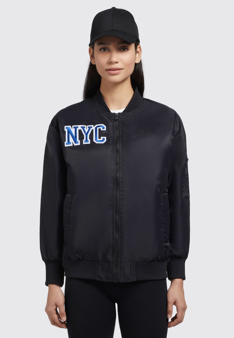 Must musta jope mustaga "NYC" embroiderimisega rinnas. Omab lukuga sulgemist, ribatud paiste ja küljetaskuid. Peakattega aksessuaarina.