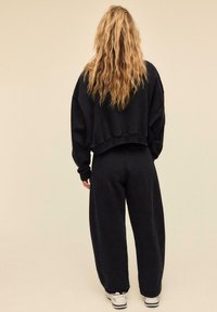 Sort cropped sweatshirt med løstsiddende ærmer kombineret med matchende bredbenede sweatpants. Materialet virker blødt og tekstureret. Hvide sneakers.