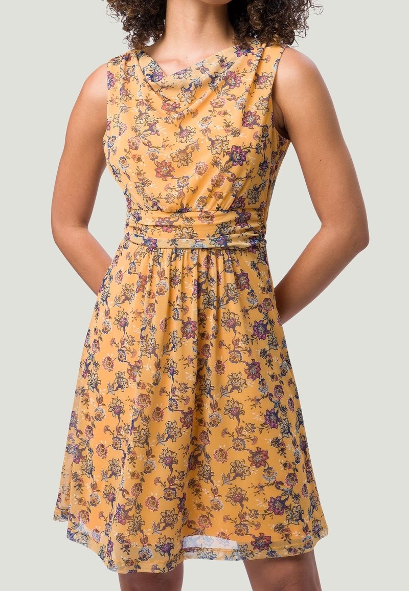 Robe jaune sans manches avec un motif floral en violet, rose et beige, présentant un col drapé et une ceinture cintrée à la taille.