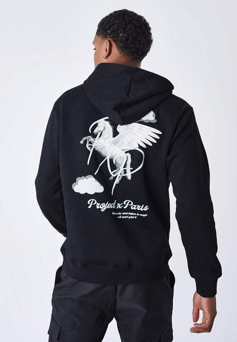 Hoodie noir en coton, arborant un graphique de licorne ailée blanche et des nuages au dos, avec du texte en police cursive.