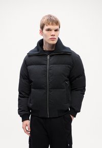 Black puffer jacket with a high collar, zip closure, and padded sections. Features side pockets and ribbed cuffs for a snug fit.