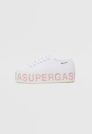 Vit dukskor med rosa blommönster på plattformen och "SUPERGA"-text. Har runda snören och metallöglor. Platt sula.