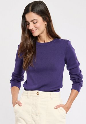 Pull en maille violet avec des manches longues, un col rond et des accents de boutons décoratifs sur les épaules. Texture lisse et design ajusté.