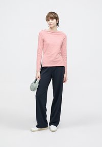 Czerwono-biały top z długim rękawem w paski w połączeniu z luźnymi granatowymi spodniami. Modelka trzyma jasnozieloną torbę i nosi białe trampki.