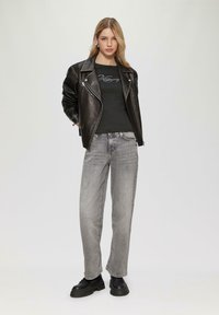 Schwarze Leder-Bikerjacke über einem dunklen, figurbetonten Oberteil, kombiniert mit hoch sitzenden grauen Jeans und klobigen schwarzen Stiefeln. Glatte Materialien und lässige Passform.