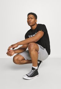 T-shirt noire avec impression "ALPHA INDUSTRY", shorts de sport gris et baskets montantes noires avec semelle et accents blancs.
