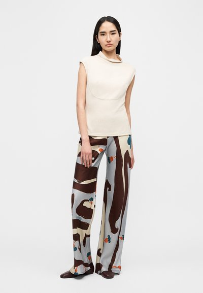 Beige ermeløs topp med sjalskrage, kombinert med mønstrede vide bukser i grått, brunt og fargerike blomsterdetaljer. Jevn tekstur.