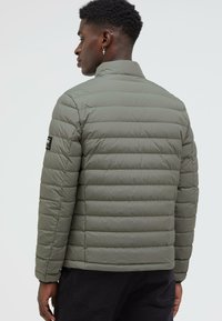 Green padded jacket with a high collar, featuring horizontal stitching and a patch logo on the left sleeve. Smooth, shiny material.